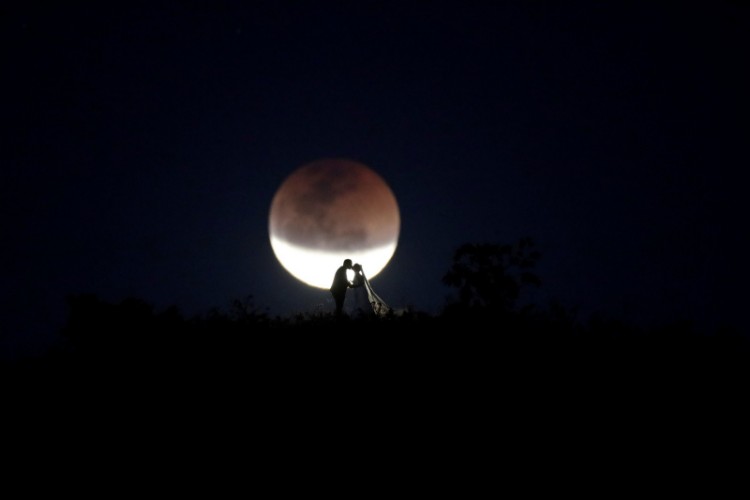 Noivos se beijam com a lua em eclipse ao fundo, em Brasília